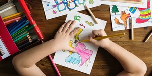 Ein Kind malt das Bild eines Malbuchbildes in bunten Farben aus. Man sieht nur die Hände des Kindes