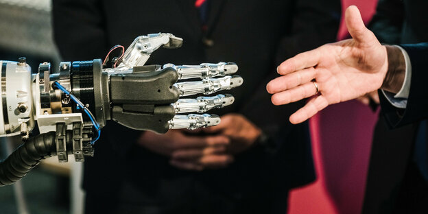 Eine menschliche und eine Roboterhand vor dem Handschlag