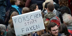 Ein Demonstrant hält ein Pappschild hoch mit der Inschrift "Forschen statt Faken"rotes gegen