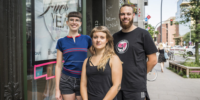 Zwei Frauen und ein Mann stehen vor dem Schaufenster ihres Sexshops.