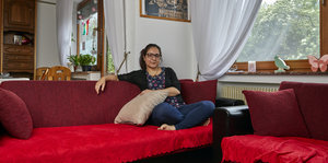Eine Frau sitzt auf einem roten Sofa und guckt in die Kamera