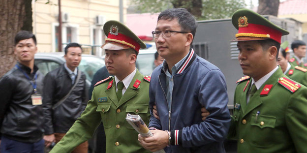 Zwei Vietnamesen in Polizeiuniform führen einen Mann in Handschellen zwischen sich