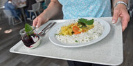 Auf einem Tablett steht ein Teller mit Reis und Gemüse, daneben ein Dessert