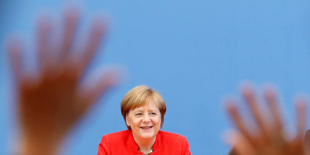 Angela Merkel lächelt, vor ihr heben sich Hände