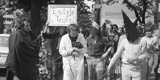 Fritz Teufel hält einen Strauß Nelken im Arm, um ihn herum Demonstranten