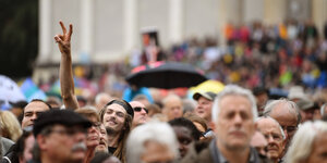 Demonstration "ausgehetzt" in München - Menschen stehen da, manche mit Regenschirm, einer hebt seine Hand