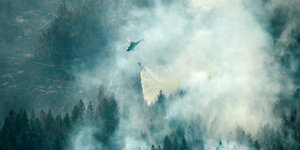 Eine Hubschrauber mit Löschwasser fliegt über einen brennenden Wald