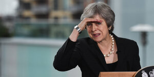 Theresa May hält sich die Hand an die Stirn, um nicht geblendet zu werden