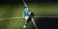 Der Fußballer Mesut Özil läuft traurig und konzentriert einem Fußball hinterher, er hat grünes Trikot an