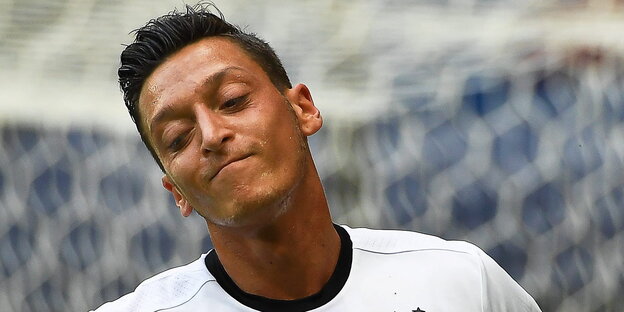 Mesut Özil steht auf dem Platz, lächelt und hat dabei die Augen geschlossen
