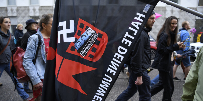 Demonstranten tragen eine Fahne. Darauf eine Figur, die ein Hakenkreuz in einen Mülleimer wirft