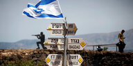 Straßenschilder in einer kargen Gegend, mit einer Israel-Fahne drauf - im Hintergrund israelische Soldaten