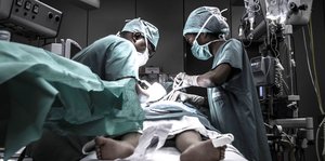 Zwei Chirurgen beugen sich über einen Menschen auf einem OP-Tisch