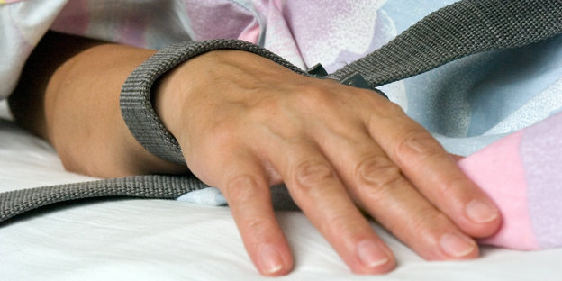 ine mit einem Textilband festgebundene Hand eines Patienten