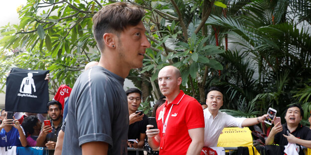 Menschen in roten T-Shirts stehen im Hintergrund, Mesut Özil trägt ein graues Shirt und wendet sich ab