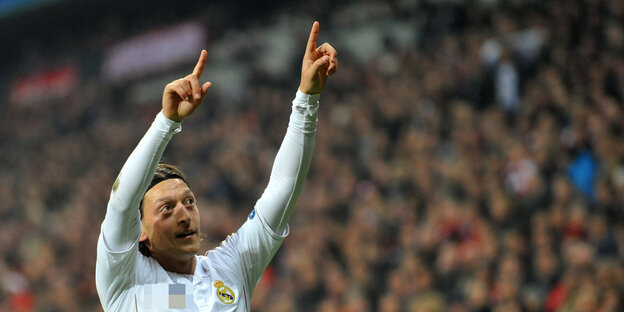 Mesut Özil steht auf dem Platz streckt beide Zeigefinger in die Luft