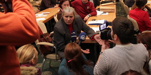 Eine Frau sitzt inmitten eines vollen Konferenzraums und spricht in Mikrofone