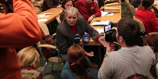 Eine Frau sitzt inmitten eines vollen Konferenzraums und spricht in Mikrofone