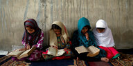 Vier afghanische Mädchen sitzen im Schneidersitz auf dem Teppich und lesen in Büchern