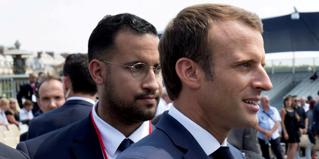 Ein Mann steht hinter einem anderen. Es sind Emmanuel Macron und sein Sicherheitsbegleiter Alexandre Benalla