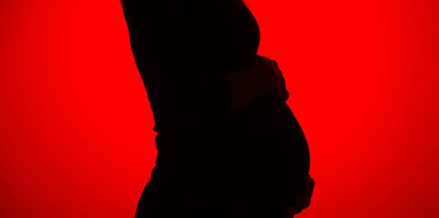 Die schwarze Silouette einer schwangern Person vor rotem Hintergrund