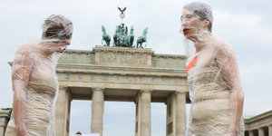 Zwei in Folie eingewickelte Frauen stehen sich vor dem Brandenburger Tor gegenüber