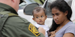Frau steht mit Kleinkind auf dem Arm vor Grenzpolizist