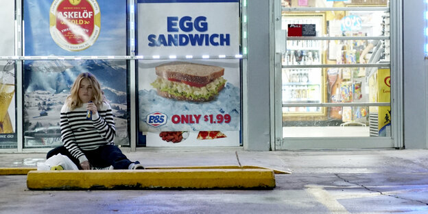 Ein Mädchen sitzt vor einem Laden und isst Schokoriegel