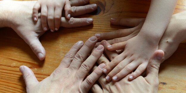 Berührende Hände auf einem Tisch: zwei Erwachsene und ein Kind