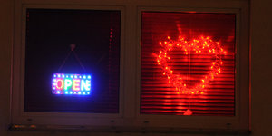 Zwei Leuchtreklamen in dunklem Fenster: Buchstaben SEX und daneben ein rotes Herz