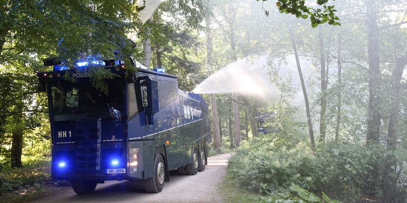 Ein Wasserwerfer fährt durch einen Park und spritzt Wasser in Bäume und Büsche