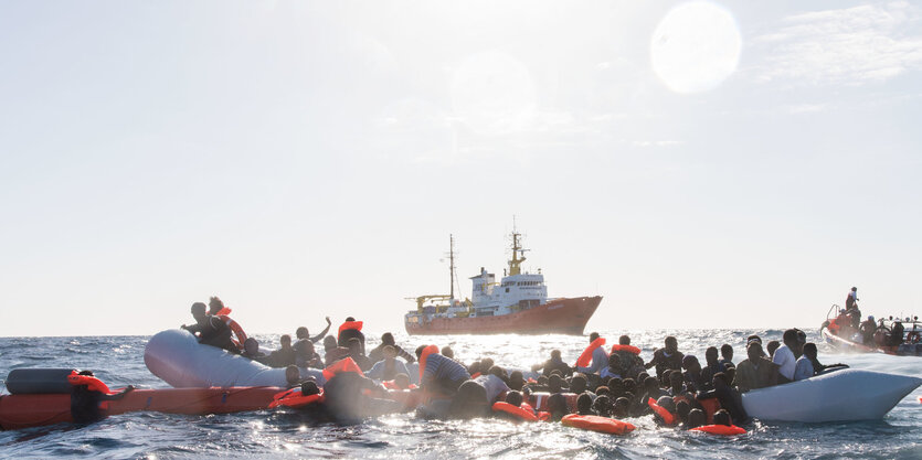 Geflüchtete auf und neben einem Schlauchboot. Einige tragen Rettungswesten