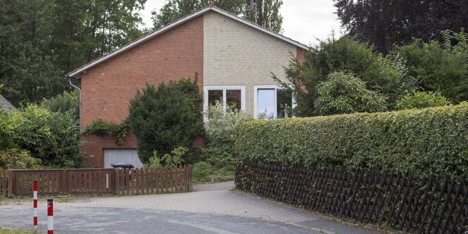 Ein älteres Haus ist von außen zu sehen, davor Hecke und Straße