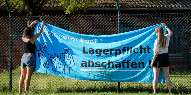 Zwei Kritikerinnen hängen ein Banner an einem Zaun auf Zwei Kritikerinnen hängen ein Banner an einem Zaun auf