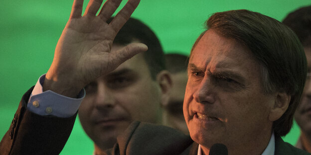 Vor einem grünen Bühnenhintergrund winkt Jair Bolsonaro in die Menge