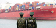 Zwei Polizisten stehen vor einem riesigen Containerschiff