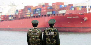 Zwei Polizisten stehen vor einem riesigen Containerschiff