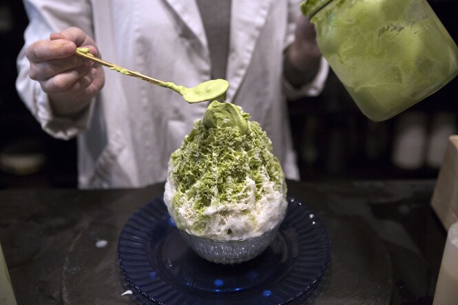 Mit einem Löffel wird grüne Sauce auf weißen Eiskristallen in einem Becher drapiert