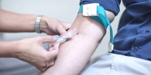 Die Hände einer Krankenschwester stechen eine Spritze in den Unterarm eines Patienten mit aufgekrempeltem Ärmel