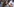 Junge Frau mit langen dunkelblauen Locken mit halberhobener Hand und Palästinensertuch um den Kopf. Im Hintergrund eine Menschenmenge