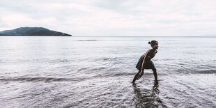 Eine junge Frau läuft an der Wasserkante zum See, im Hintergrund eine Insel