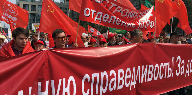 Demonstranten stehen vor einem Transparent mit der Aufschrift „Für echte Gerechtigkeit!“, außerdem werden Fahnen der Sowjetunion und der Kommunistischen Partei der Russischen Föderation geschwenkt