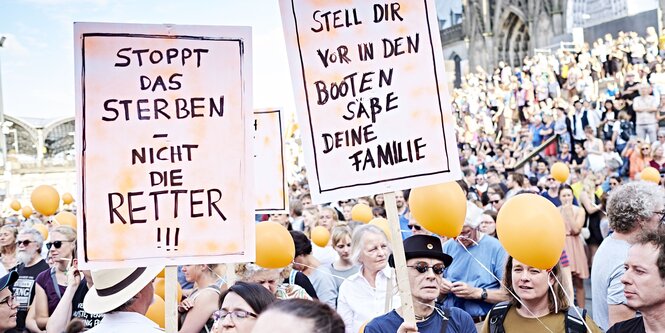 Demonstranten halten Schilder mit den Aufschriften „Stoppt das Sterben - nicht die Retter!“ und „Stell dir vor, in den Booten säße deine Familie“ hoch