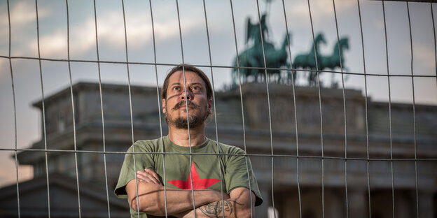 Erk Acarer steht vor dem Brandenburger Tor und verschränkt die Arme