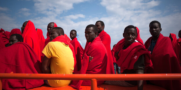 Auf einem Rettungsboot sitzen in Decken gehüllte Flüchtlinge