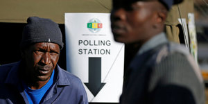 Wahl in Simbabwe - zwei Männer stehen vor einem Schild, auf dem "Polling Station" (Wahllokal) steht
