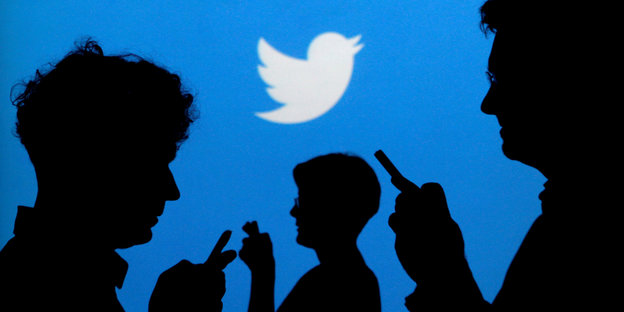 Ein Schattenriss von drei Menschen, die Smartphones in der Hand halten, vor einer Wand mit dem Twitter-Logo