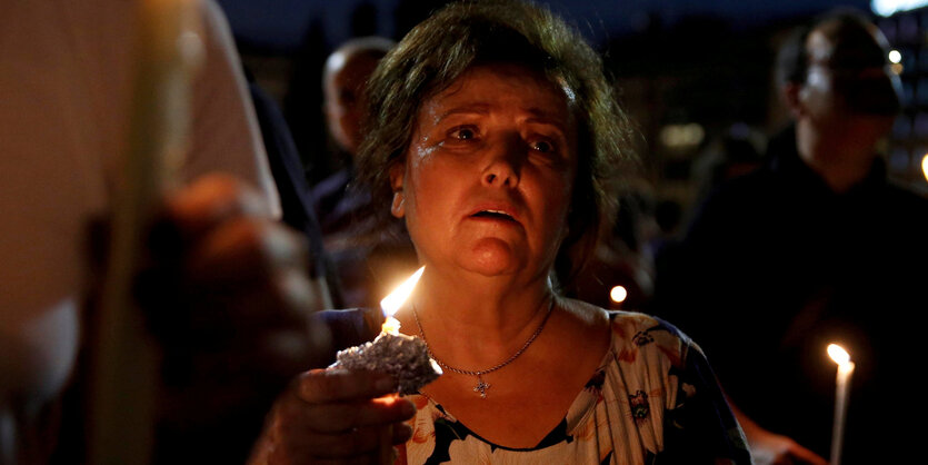 Eine Frau hält bei einer Trauerfeier für die 91 Toten nach Waldbränden in Athen eine Kerze