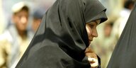 Eine iranische Frau mit Hijab. Unscharf im Hintergrund ein Mann, der in ihre Richtung schaut
