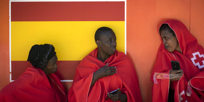 Drei Frauen stehen an einer Wand. Sie sind in Decken gehüllt